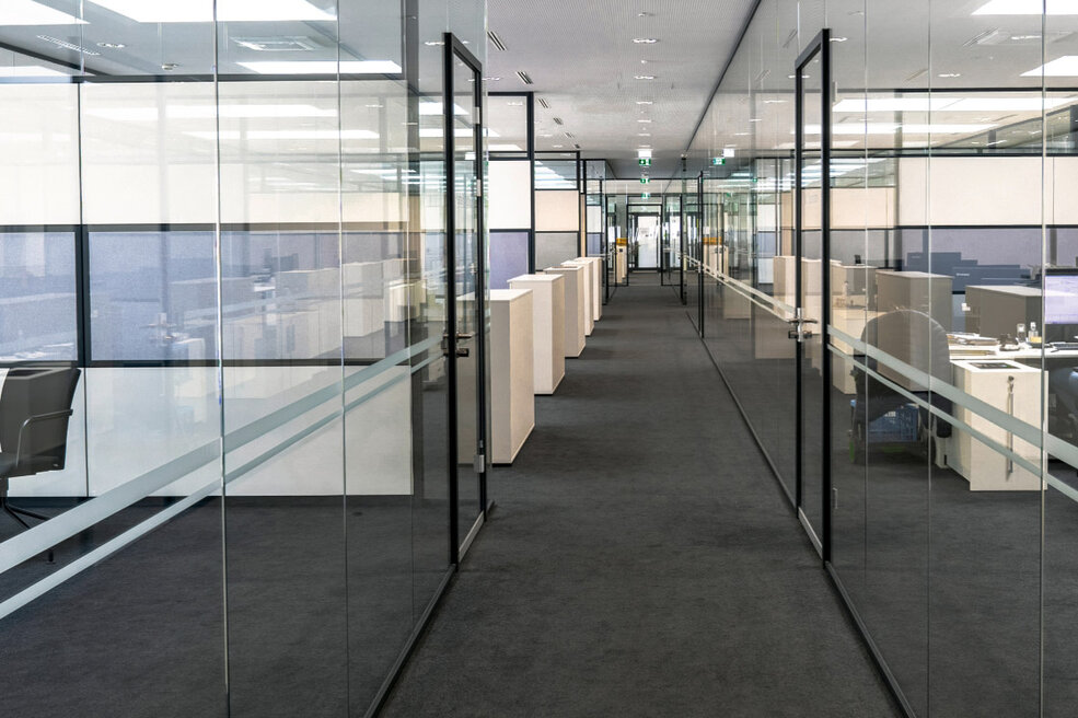 JOKA-Referenzen-Teppich-Büro Flur eines gläsernen Büros im Autohaus, in dem der dunkelgraue JOKA Format Teppichboden verlegt ist.