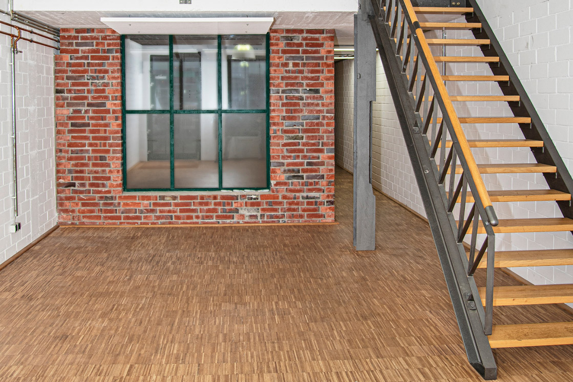 Ein Raum mit einer Ziegelwand und einer Metalltreppe, die auf einen hellen Parkettboden trifft, was eine industrielle und moderne Atmosphäre schafft.