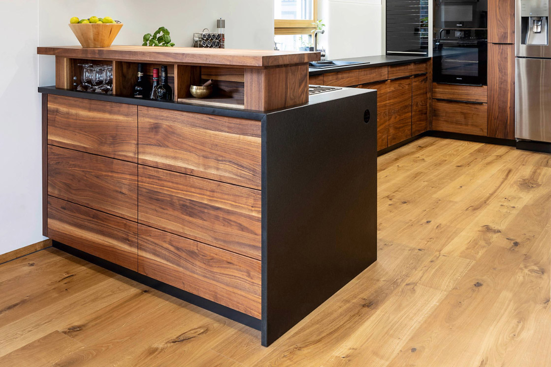 Eine moderne Küche mit einer freistehenden Kücheninsel aus Holz und dunklem Metall. Der warme Holzfußboden sorgt für ein harmonisches Gesamtbild.